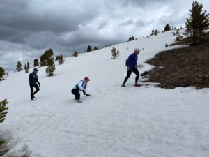 three runners on a snow-covered mountain, with one has a leg in the snow.