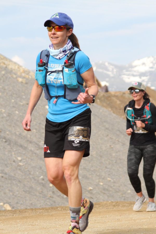 two female runners, one in foreground, one in background above treeline with a snow-capped mountain in the background