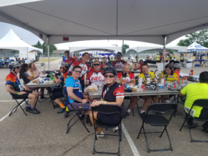 Cyclists sitting at tables under an event tent having lunch