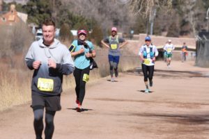 Runners on a wide flat dirt trail during winter. The man in front has a pained look on his face. 