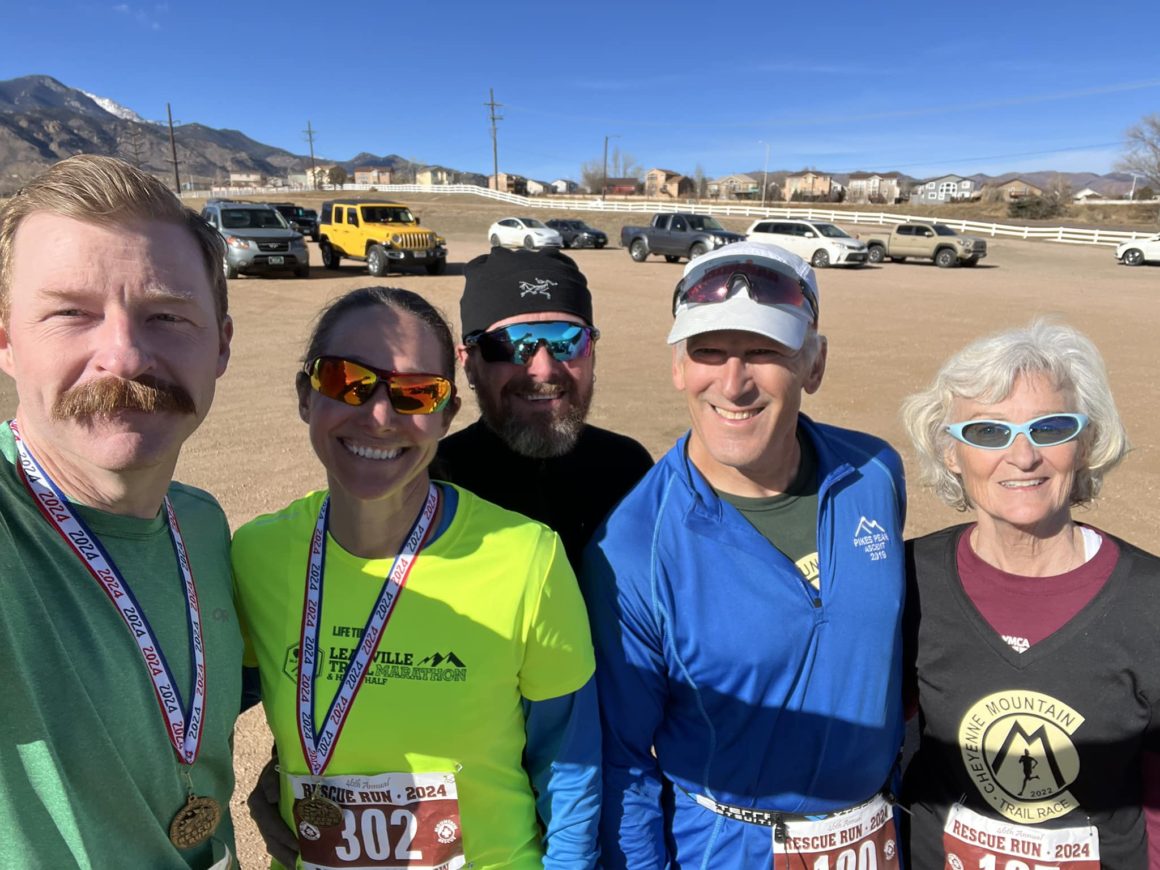 Selfie of 5 white runners (three male, two female) in a dirt parking lot.